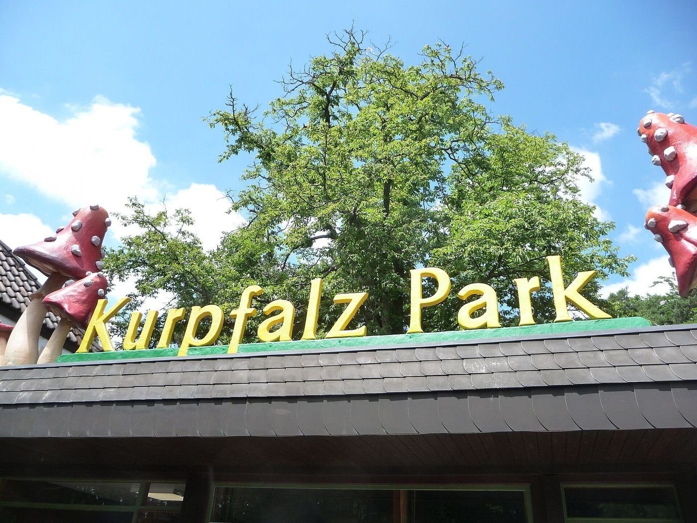 Eingang des Kurpfalz-Parks mit gelbem Schriftzug und Pilzfiguren auf dem Dach